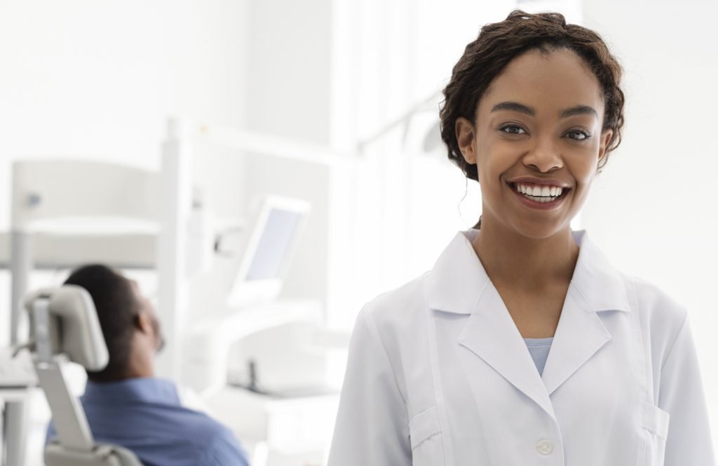 Portrait of cheerful female dentist with a male patient in the background