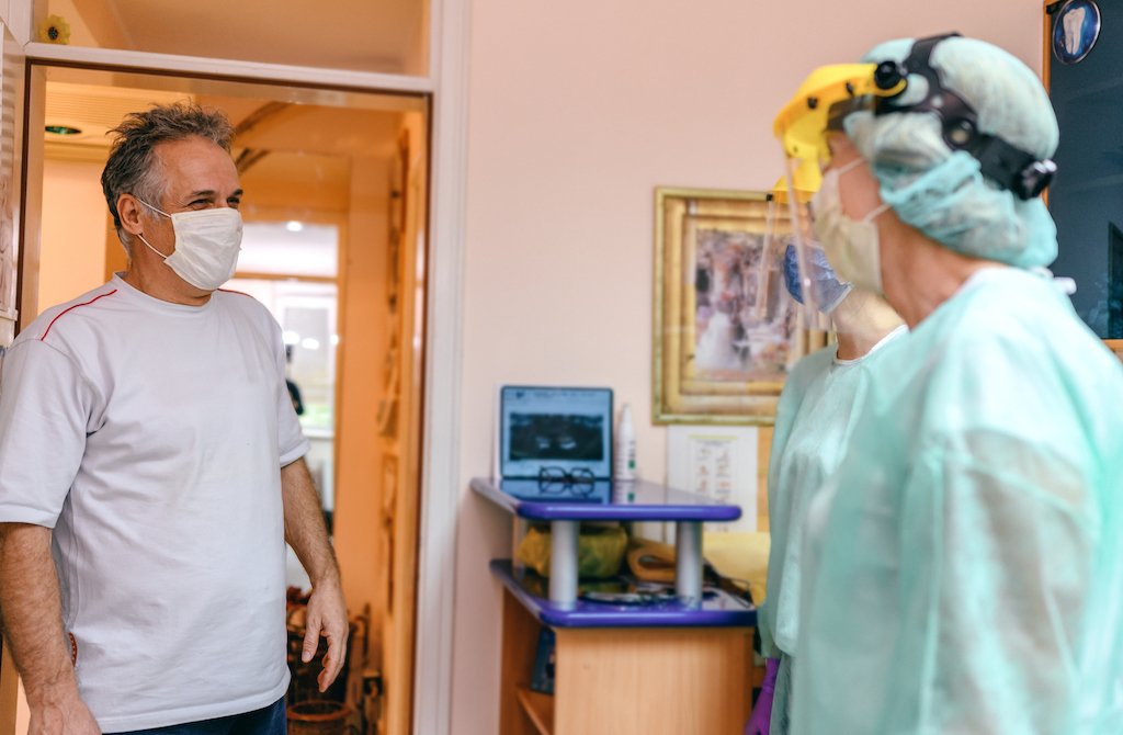 Dentist in PPE greeting patient wearing a mask