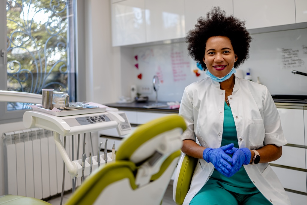 A smiling dentist sitting in an empty dental exam room